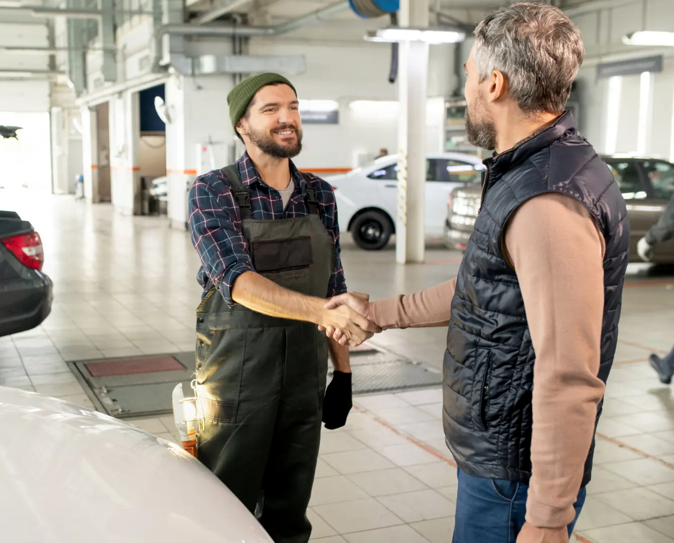 A mechanic and a customer shaking hands inside a garage.
